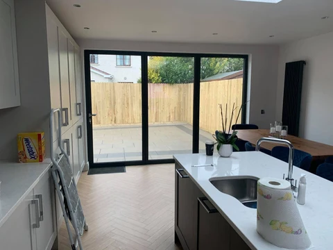 Kitchen interior looking out through closed anthracite bifold doors to a paved courtyard, herringbone floor