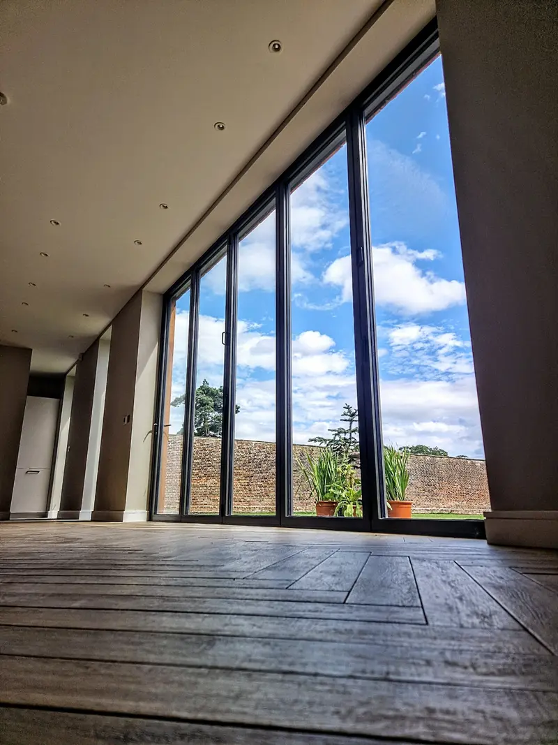 Floor-to-ceiling anthracite bifolds, closed, in an empty plank-floored room, walled garden beyond