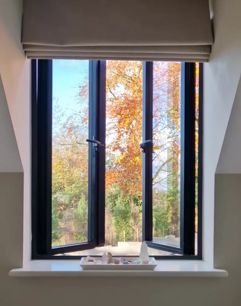 Anthracite aluminium casement pair open from inside, autumn woodland beyond