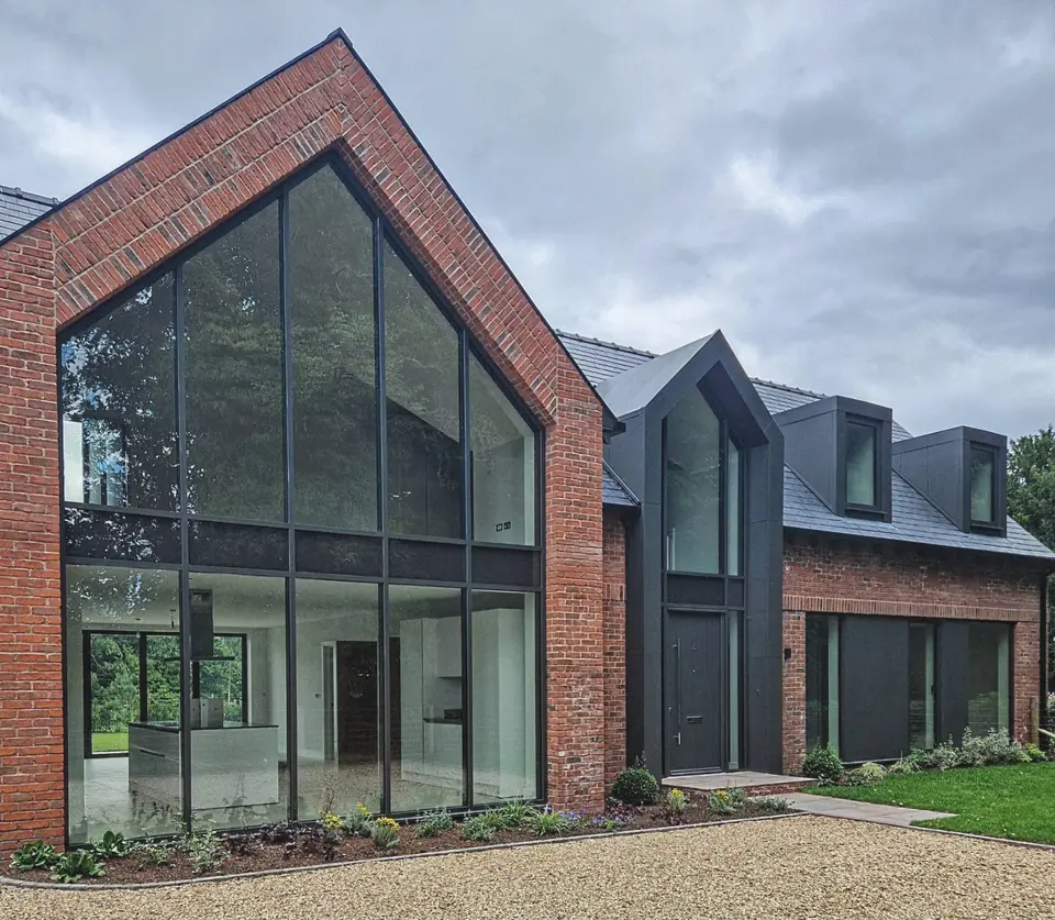 Full-height black aluminium glazed gable in a red-brick house, beside a dark second gable and dormers