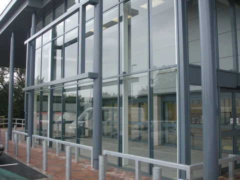 Grey aluminium curtain walling to a commercial unit, bollards and car park outside