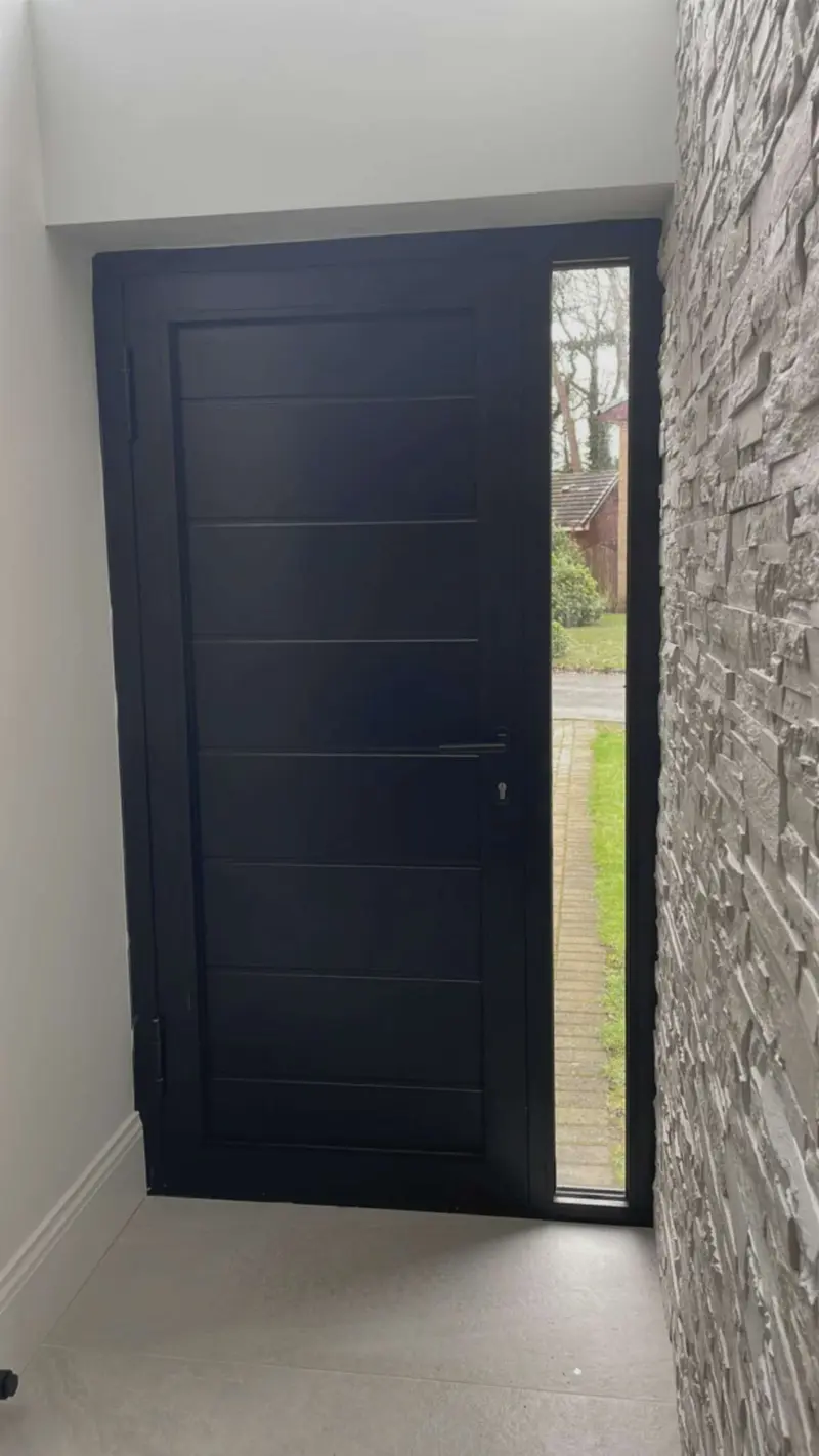 Closed anthracite front door and glazed sidelight in a hallway with split-face stone cladding