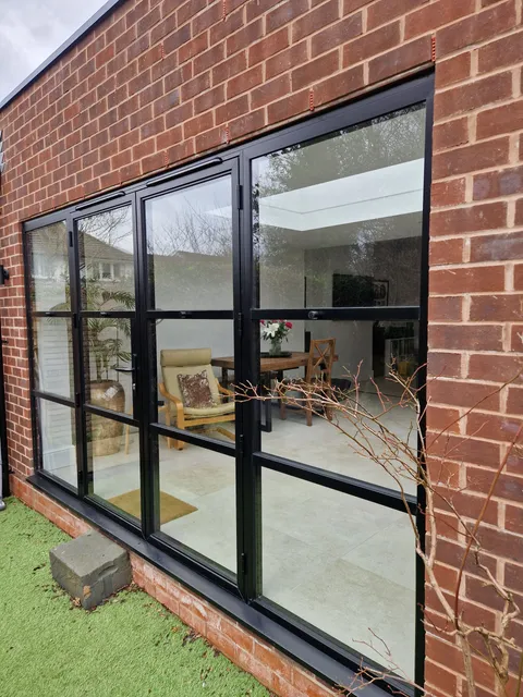 Black steel-look aluminium doors and side screens in a red-brick garden extension, seen from the lawn