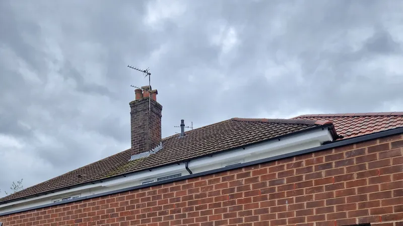 Tiled roofline of a brick house with a chimney stack, TV aerial and white fascia and guttering