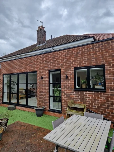 Black aluminium windows and Crittall-style doors set in red brickwork, seen across a patio garden