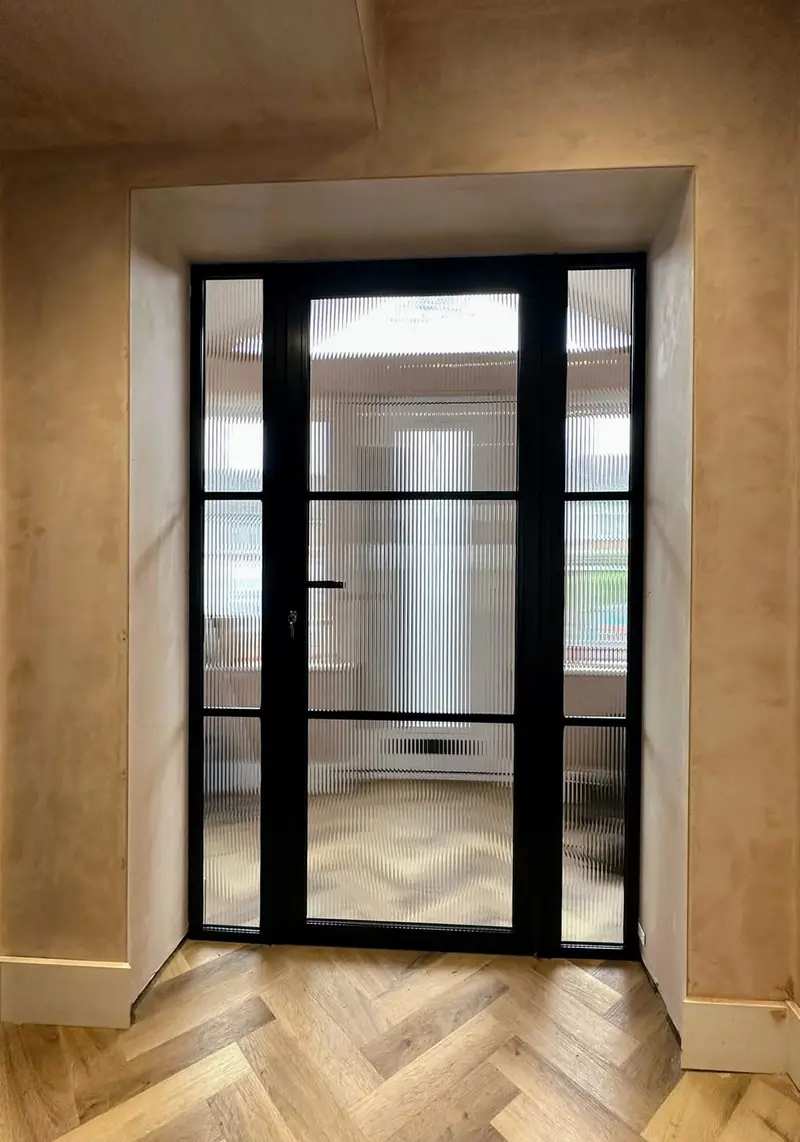 Black steel-look internal door with reeded-glass sidelights, set in a plaster reveal above herringbone parquet