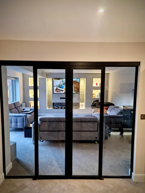 Black-framed internal glazed doors, closed, between a hall and a grey-toned living room