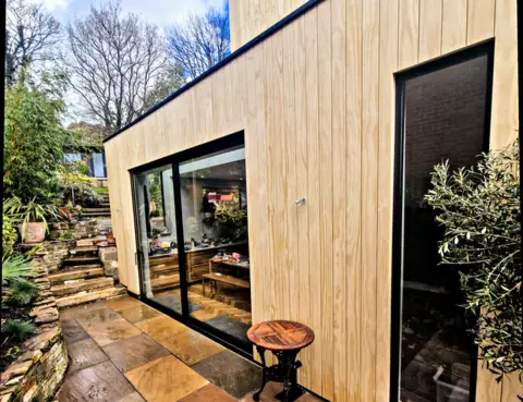 Black aluminium sliding doors, closed, in a timber-clad garden room above a sandstone patio